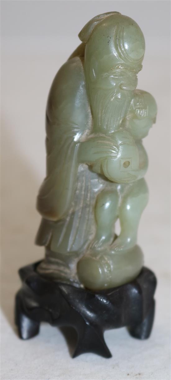 A Chinese celadon and brown jade group of Shou Lao and a boy standing upon a barrel, 18th/19th century, 7.3cm, ebonised wood stand